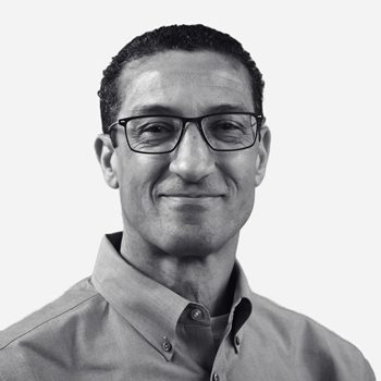 Man wearing glasses, smiling, in button-up shirt.