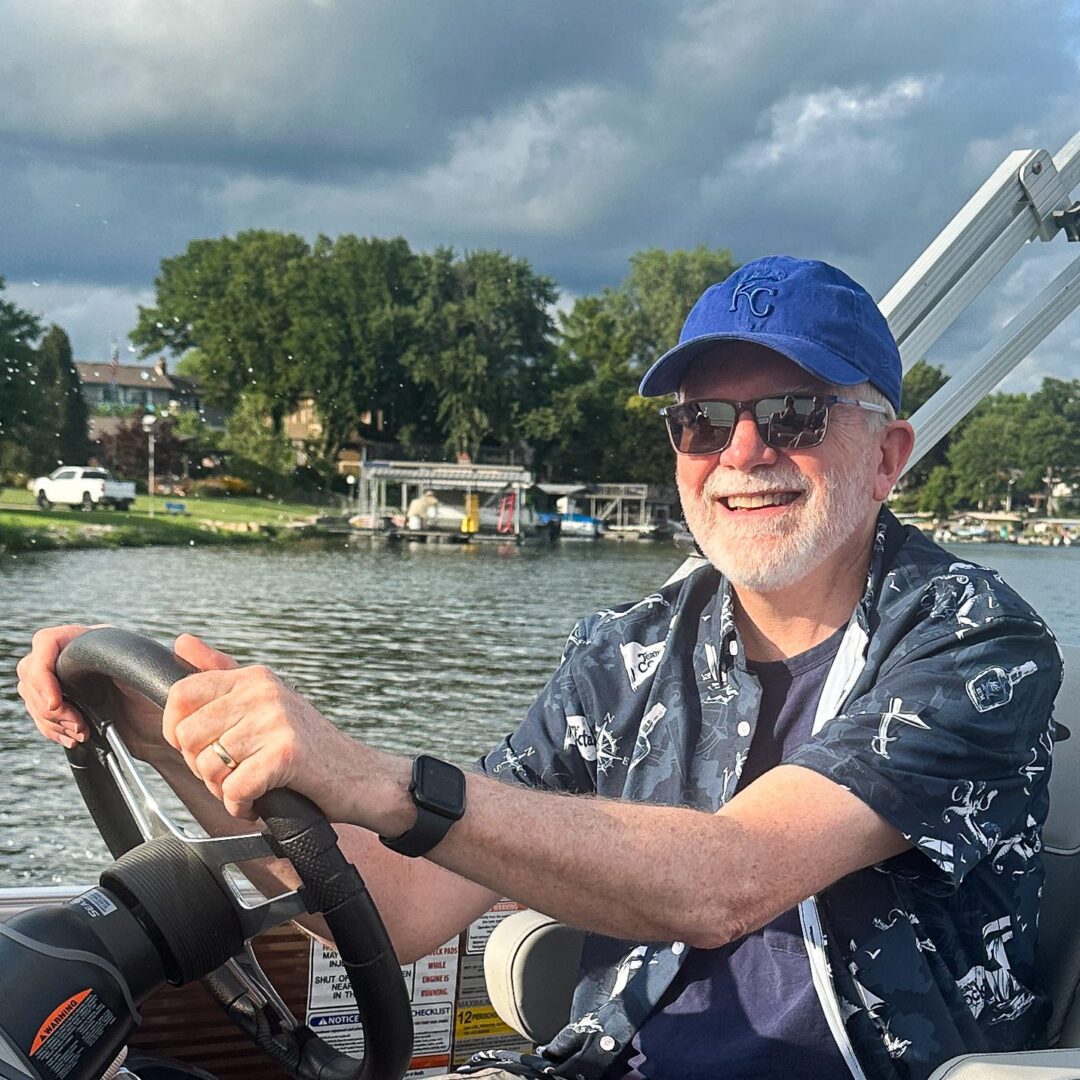 Man steering a boat on a lake, smiling under a cloudy sky.