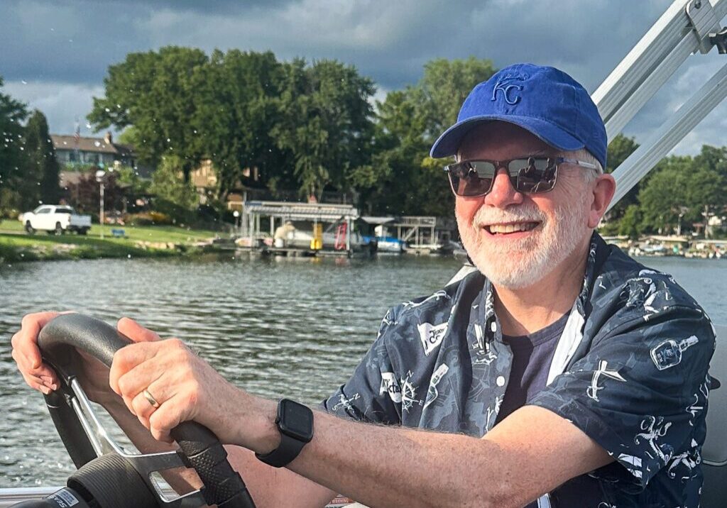 Man steering a boat on a lake, smiling under a cloudy sky.