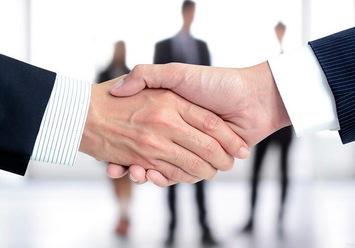 Two people shaking hands with blurred business team in background.